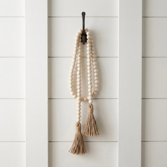 Decorative wall hanging with beads and tassels on a white wooden panel background